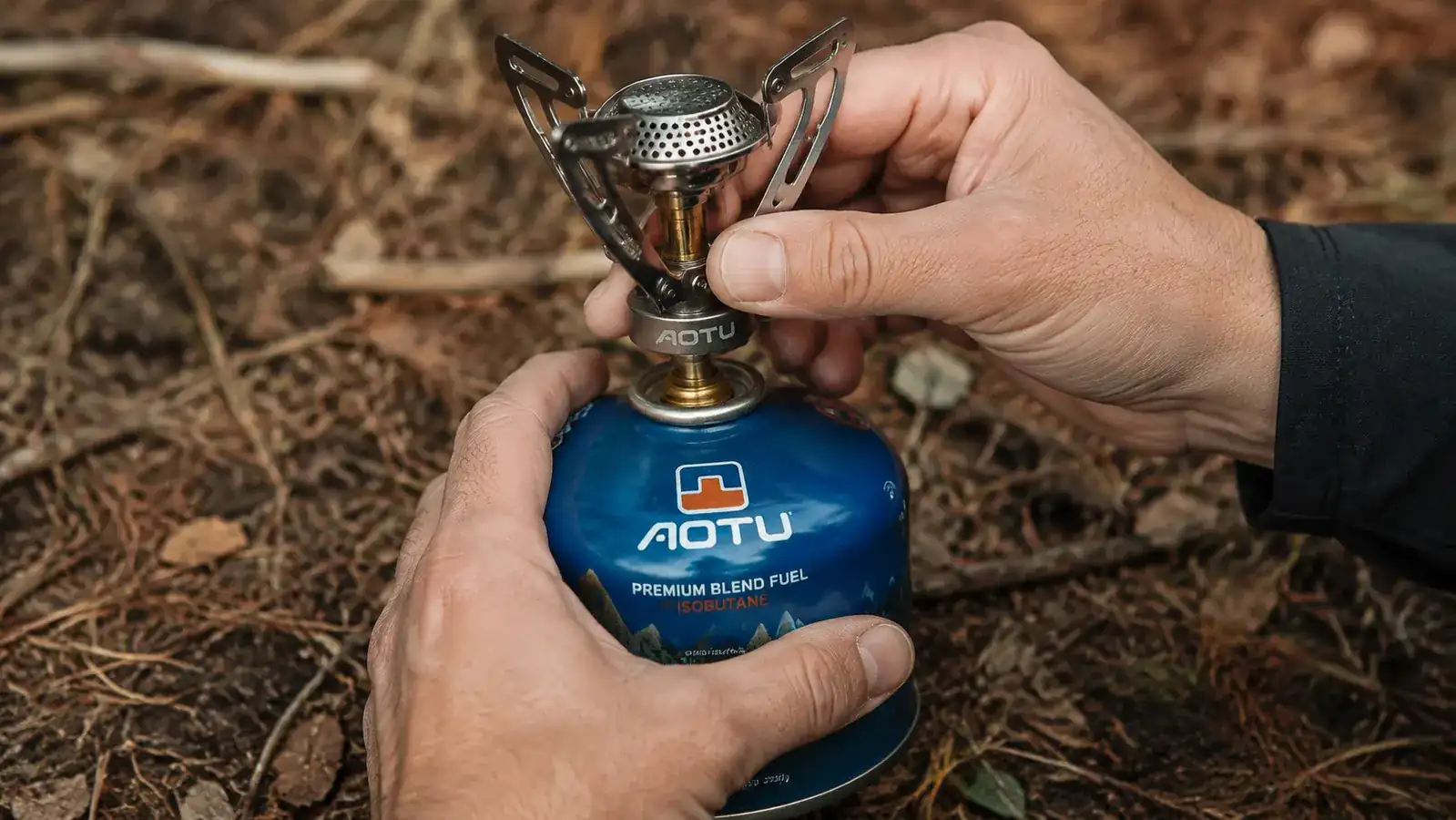 Hand threading a canister stove onto a small isobutane fuel canister at a campsite