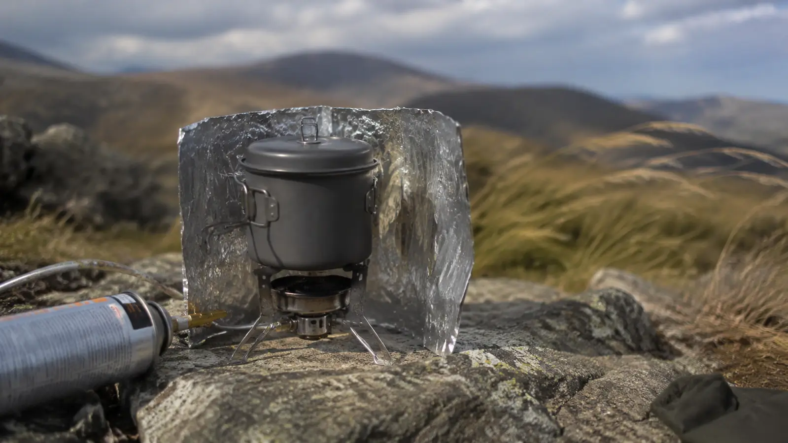 Wind screen improvised from aluminum foil wrapped around a backpacking stove on a windy ridgeline