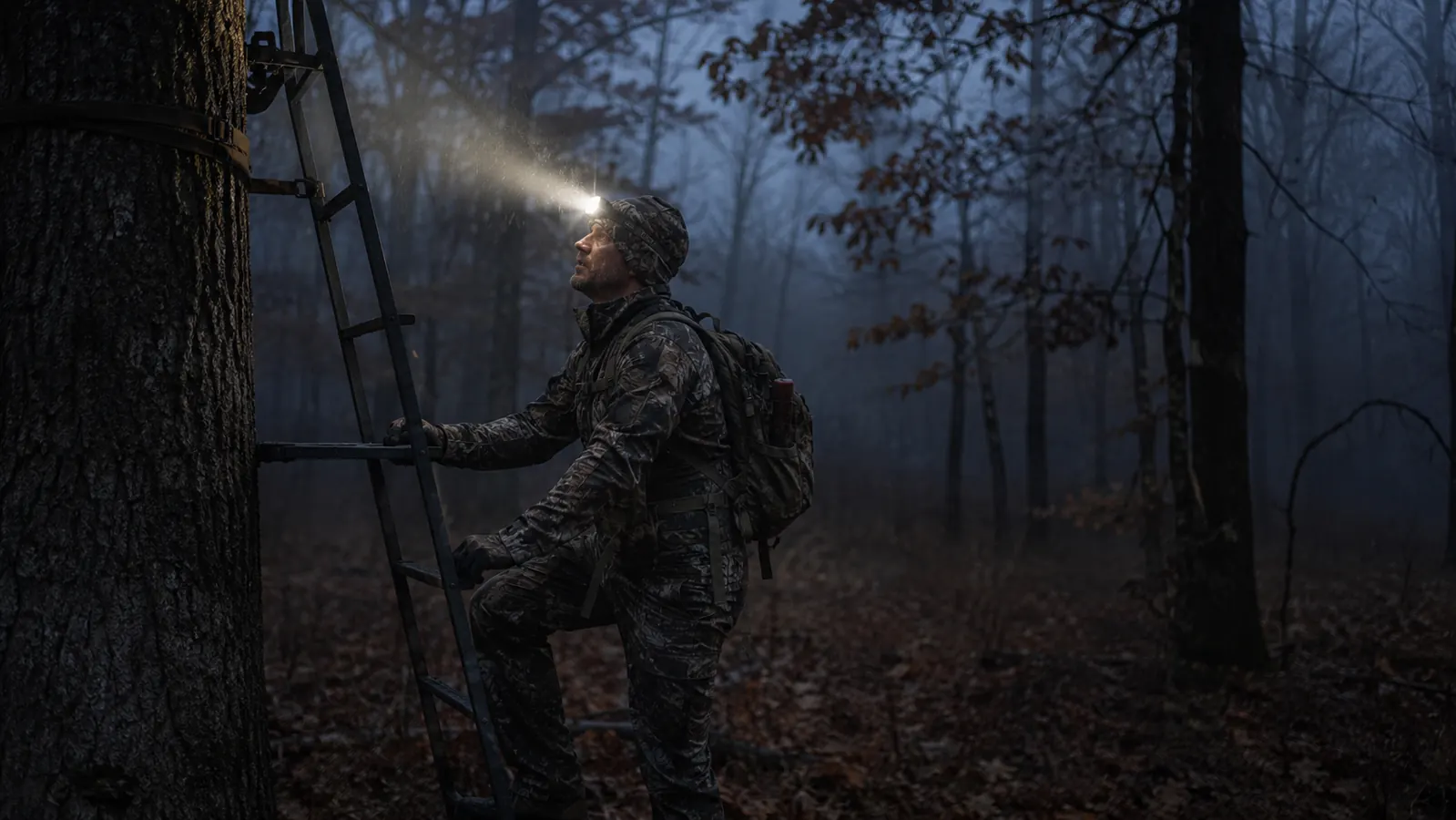 Hunter in pre-dawn darkness wearing a headlamp while setting up a deer stand