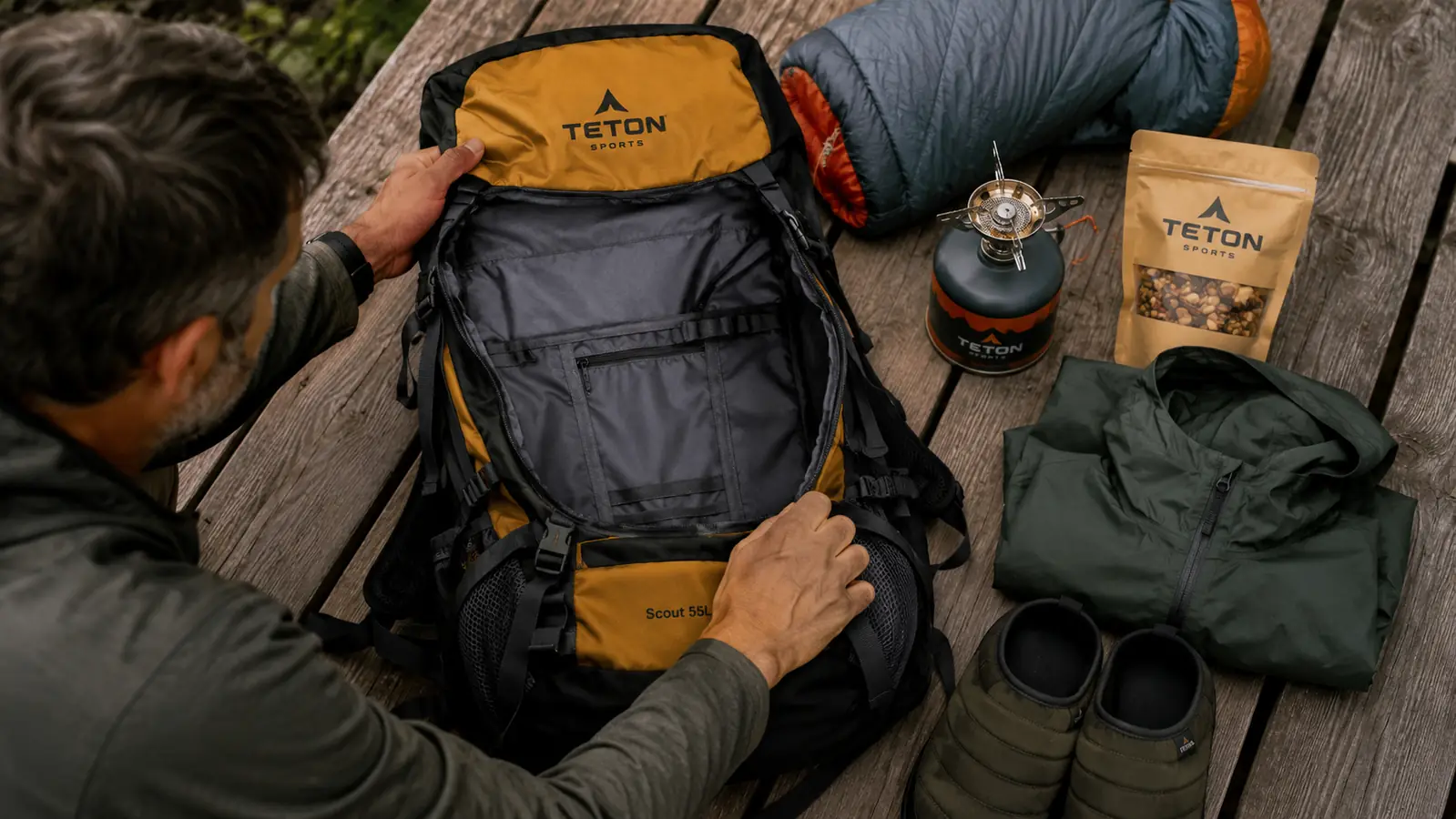 Gear laid out flat on a tarp next to an open backpack, organized into sleeping system, food bag, and clothing layers before packing