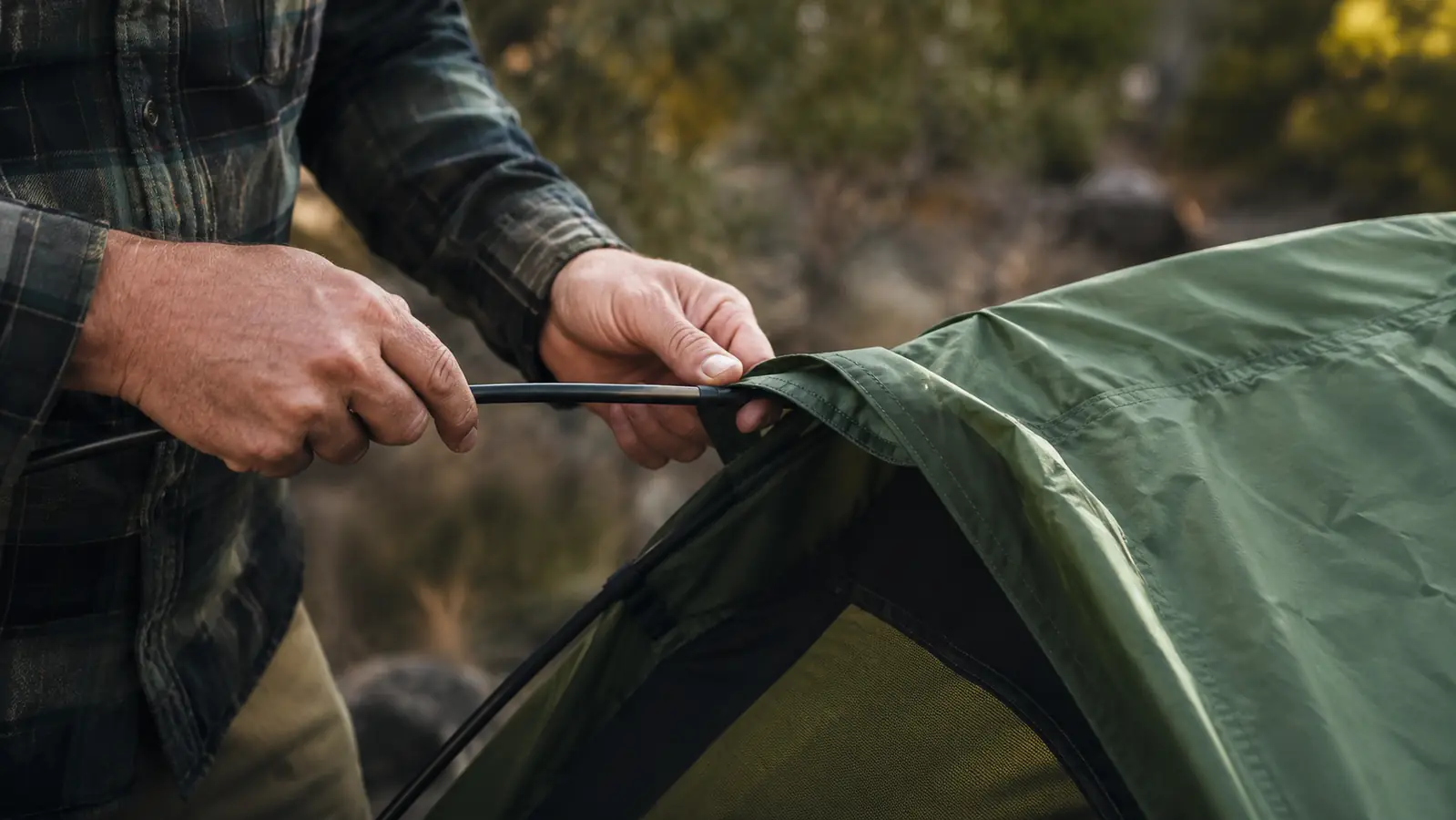 Close-up of CORE dome tent poles being threaded through fabric pole sleeves, hands visible working the flexible fiberglass rod